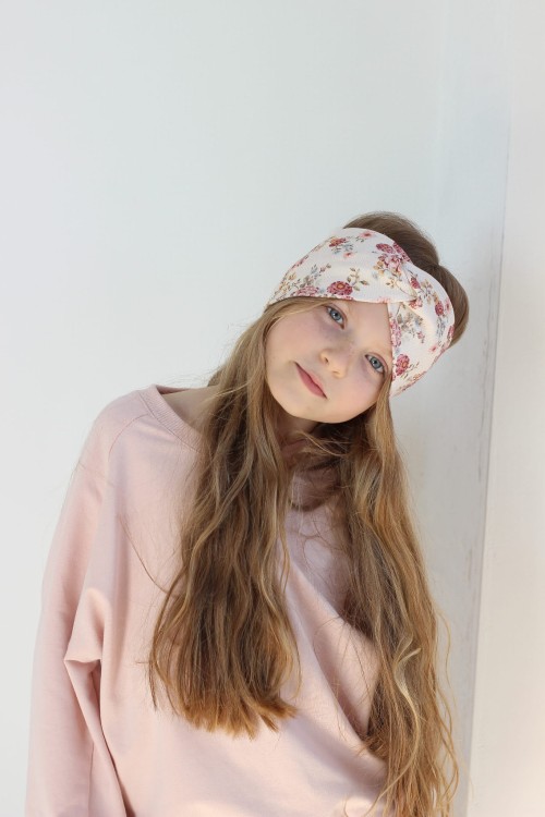 Dziewczynka w opasce przeplotce Bloom w kwiaty na biszkoptowym tle.